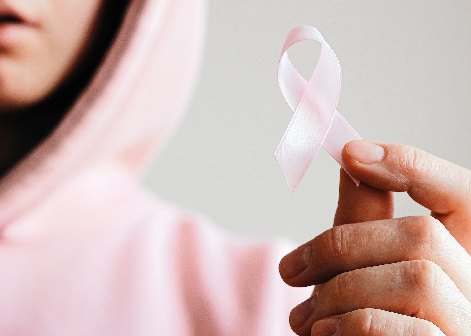 A woman in a pink hoodie holds up a pink ribbon