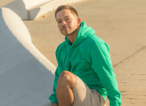 A man wearing a green hoodie sits on a bench