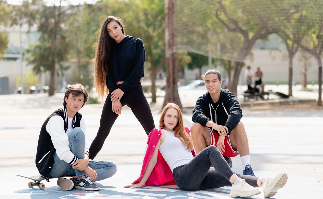 4 young people posing for the camera, wearing clothes which include a varsity jacket, and a cropped hoodie