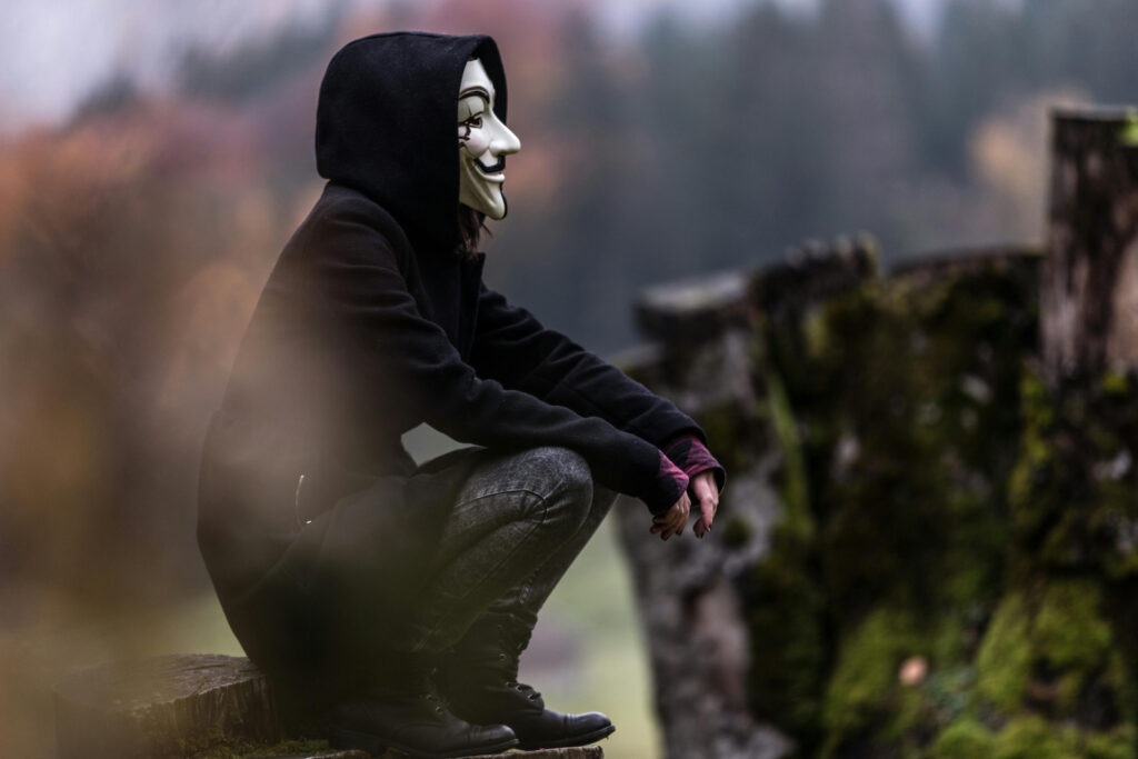 A person wearing a hoodie and an anonymous mask