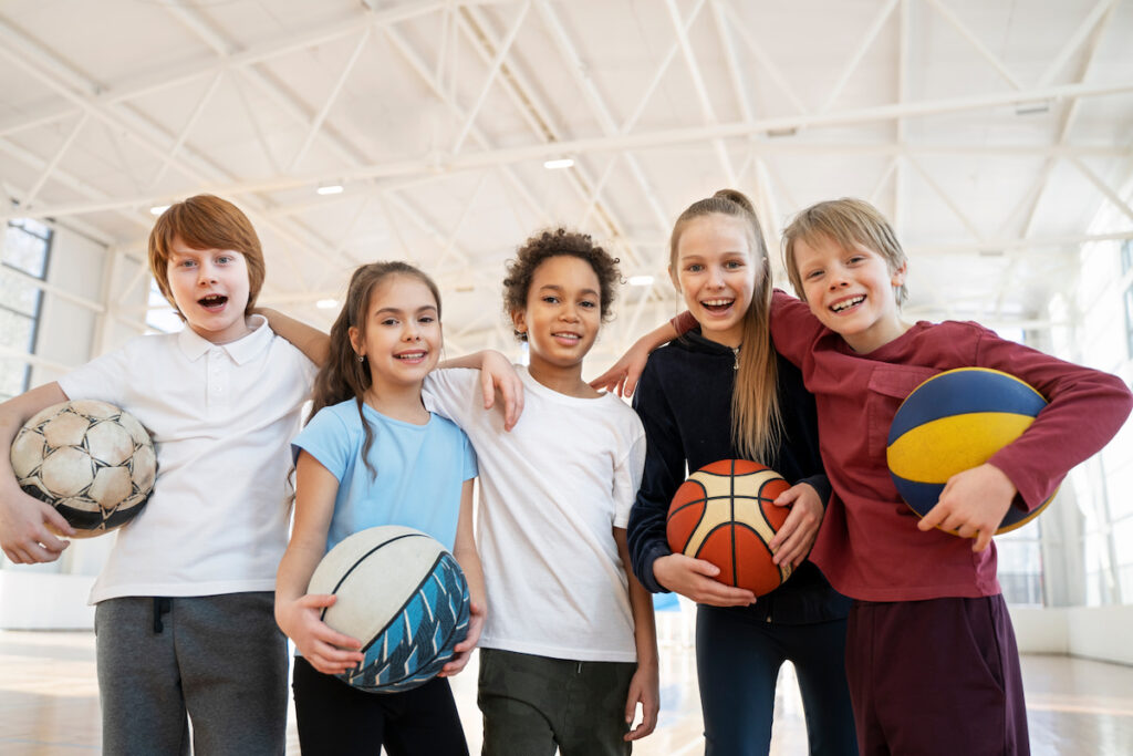 A group of children holding footballs and basketballs