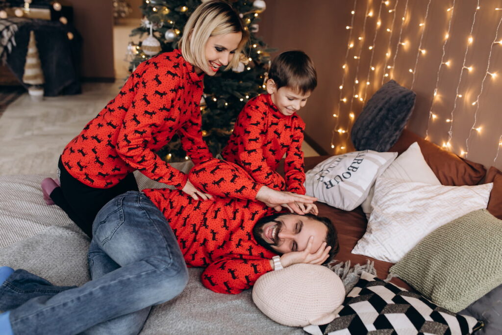 A mother and young son dragging the father out of bed at Christmas