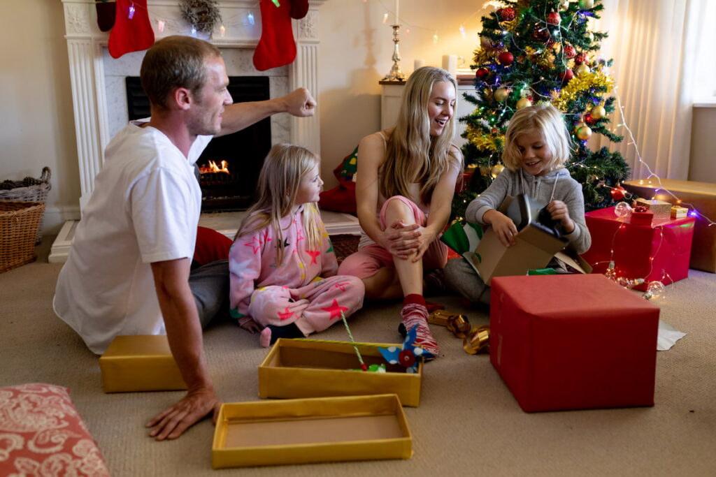 A family in pajamas sit on the lounge floor and open presents